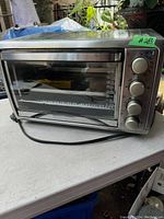 Stainless steel Black & Decker toaster oven with glass front and control knobs on the right, sitting on a table outdoors.