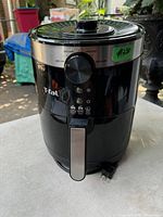 Full view of T-Fal air fryer showing front dial control, brand logo, and power cord plugged in, placed outdoors.