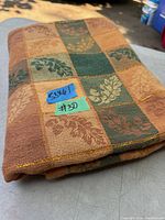 Folded vintage cotton tablecloth with checkered leaf pattern in warm tones, outdoor setting.