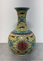 Front full view of the hand painted Chinese ceramic vase showing the bulbous body, decorated with red Shou symbols and floral motifs on yellow background with blue accents.