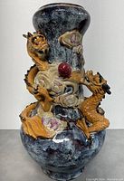 Front view of the vase showing dual 3D dragons entwined around neck and body, with red orb and swirling patterns on blue-black mottled ceramic.