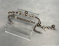 Two 925 silver bracelets displayed on a clear stand, showing length and charm details.