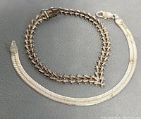 Two silver bracelets on dark grey surface showing length and clasp details.