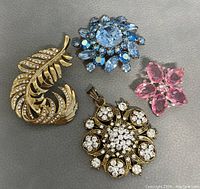 Five vintage rhinestone brooches laid out on gray surface showing various designs and colors.