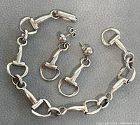 Silver bracelet and matching earrings on grey textured background, highlighting horse bit link design and 925 markings.