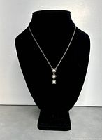 Full front view of necklace displayed on black mannequin stand showing silver chain and pendant with three pearl-like flowers hanging vertically.