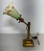 Side view showing the trumpet-shaped glass shade on the brass adjustable arm and square base. Power cord attached.