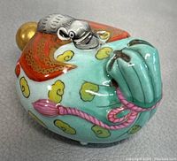 Top and side views of a hand painted porcelain perfume bottle featuring an elephant head design with gold, turquoise, red, and pink accents captured on a neutral surface.