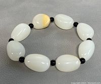 View of the bracelet laid flat showing the oval white jade beads with one bead having yellowish coloration and the black spacer beads in between.