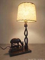 Full view of the table lamp turned on showcasing its fiberglass shade and the gazelle base sculpture.