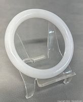 Front view of natural white jade bangle on clear display stand showing round shape and smooth surface.
