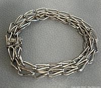 Photo showing the bracelet folded into an oval shape on gray background, highlighting the triple chain elongated links and box clasp.