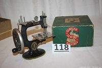Child-size Singer sewing machine displayed with original green box and a white number 118 card beside them.