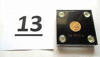 Coin in black plastic display with “LG. GOLD $” label alongside lot number card