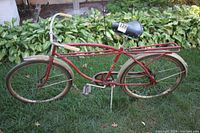 Side view of vintage red bicycle with 26" wheels, dirt on tires, and attached rear rack.