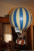 Full view of large hot air balloon model with blue and white stripes and net overlay, suspended showing basket below.