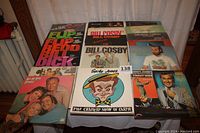 Photo showing all 17 comedy records arranged on a table, featuring Flip Wilson, Bill Cosby, George Carlin, All in the Family, Spike Jones, Abbott and Costello, and Here's Johnny albums.