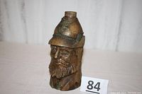 Front view of the bottle shaped as a bearded man’s head wearing an Italian alpine soldier hat with eagle.