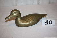 Side view of brass duck figurine showing overall shape, posture, and felt bottom.