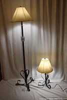 Photo of both lamps together showing the floor lamp standing on an iron base with curled feet and the smaller table lamp next to it with the same base style.