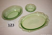 Three green glass pieces displayed: oval Hazel Atlas serving dish, small round Jeannette bowl, and larger oval Anchor Hocking platter.