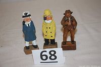 All three hand carved wooden figurines are displayed standing in a row on a neutral cloth background next to a lot number card.