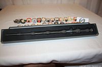 Photo showing the Dumbledore wand in its black display box with 24 Harry Potter Funko Pop! vinyl figures arranged in two rows on a table behind it.