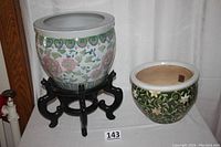 Front view of two ceramic planters together on a white cloth background showing the larger Asian design planter on black wooden stand and smaller green planter beside it