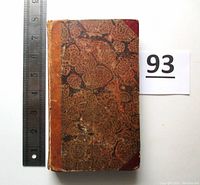 Top view of the book closed showing worn mottled brown and red cloth cover with leather spine and corners, alongside a ruler for size reference showing about 7.25 inches height.