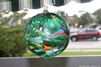 Front view of glass ball showing embedded colorful spots and smooth round shape.