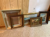 All items included in lot arranged on carpet against wood panel wall: two framed unsigned oil paintings, one framed Mexico souvenir print, two large empty frames.
