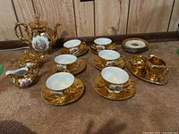 Photo showing teapot, 6 cups and saucers, cream and sugar bowls, and plates arranged on carpeted floor
