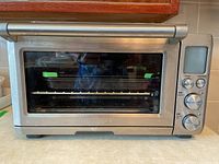 Front view of stainless steel Breville Convection Smart Oven showing glass door and metal handle with two trays inside.