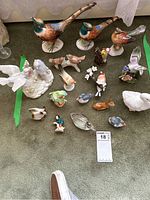 Overview of various collectible bird and animal figures displayed on a carpeted floor, including pheasants, songbirds, a swan, a rabbit, and more.