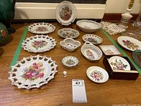 Full lot of vintage pierced and laced-edge china plates, bowls, and thimble arranged on a wooden table.