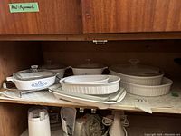 Shelf with five ceramic casserole dishes including three CorningWare Cornflower Blue casseroles and two French White casseroles, all with glass lids