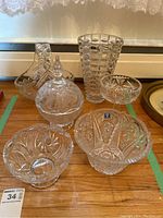Photo showing the entire lot of six crystal items on a wood surface against a window, including vase, pedestal dish with lid, basket, and bowls