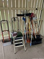 Full view of garage and garden tools arranged against a fence, showing all items included in the lot