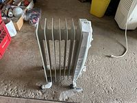 Front angle view of white Garrison oil heater showing six fins and attached feet on concrete floor.