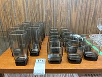 Arrangement of 11 high ball glasses and 12 short glasses on a wooden surface with a wood grain wall in the background.