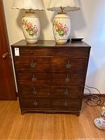 Full frontal view of the wooden highboy dresser showing all five drawers and floral lamps on top.