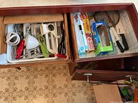 Overview of two kitchen drawers with assorted kitchen tools including cutting board, plastic wrap boxes, and utensils.