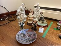 Group shot showing various figurines on a wood floor with an illustrated plate in front; includes man and woman bisque porcelain figures with baskets.