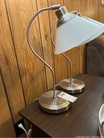 Pair of IKEA desk lamps side by side on wooden surface, showing curved chrome necks and weighted chrome bases with conical white glass shades.