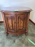 Front view of one Craftline round wooden side table showing carved double doors and rounded feet.