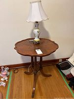 Full view of the veneer pie crust edge table showing table top, legs, and lamp on top.