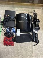 Photo showing both PS2 and PS3 consoles with all controllers and charging dock arranged on carpet