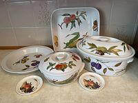 Full set of Royal Worcester Evesham M series porcelain cookware and serving dishes arranged on a countertop, showing fruit designs on white porcelain.