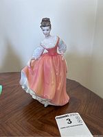 Front view of the Royal Doulton porcelain figurine depicting a woman in a peach dress, holding the dress and showing detailed face and upper body.
