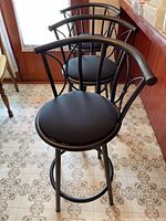 Three black metal swivel bar stools lined up showing the front and side view of the padded seats and backrests with curved metal design.